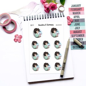 May include: A sheet of stickers featuring a woman with brown hair and a blue dress holding a glass of water. The stickers are round and have a white background. The text "Vaalea & Tumma" is printed on the sheet.