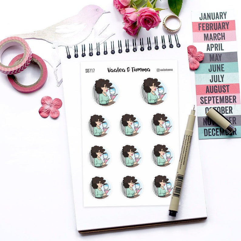 May include: A sheet of stickers featuring a woman with brown hair and a blue dress holding a glass of water. The stickers are round and have a white background. The text "Vaalea & Tumma" is printed on the sheet.