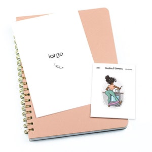 May include: A pink spiral bound notebook with a white page showing the word "large" and a sticker of a woman in a teal and pink outfit cooking on a stove. The sticker has the text "Vaalea & Tumma" on it.