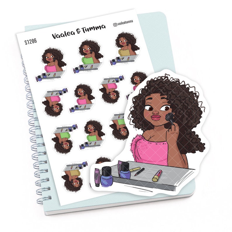 May include: A sheet of stickers featuring a cartoon illustration of a woman applying makeup. The woman has brown skin, curly black hair, and is wearing a pink shirt. The stickers are on a blue and white spiral notebook. The text "Vaalea & Tumma" is printed on the notebook.