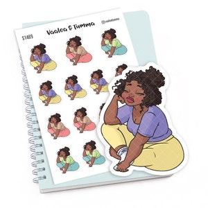 May include: A sheet of stickers featuring a cartoon illustration of a woman with brown skin and curly hair sitting with her chin on her hand. The stickers are on a white background with a blue spiral bound notebook in the background. The text "Vaalea & Tumma" is printed on the sheet of stickers.