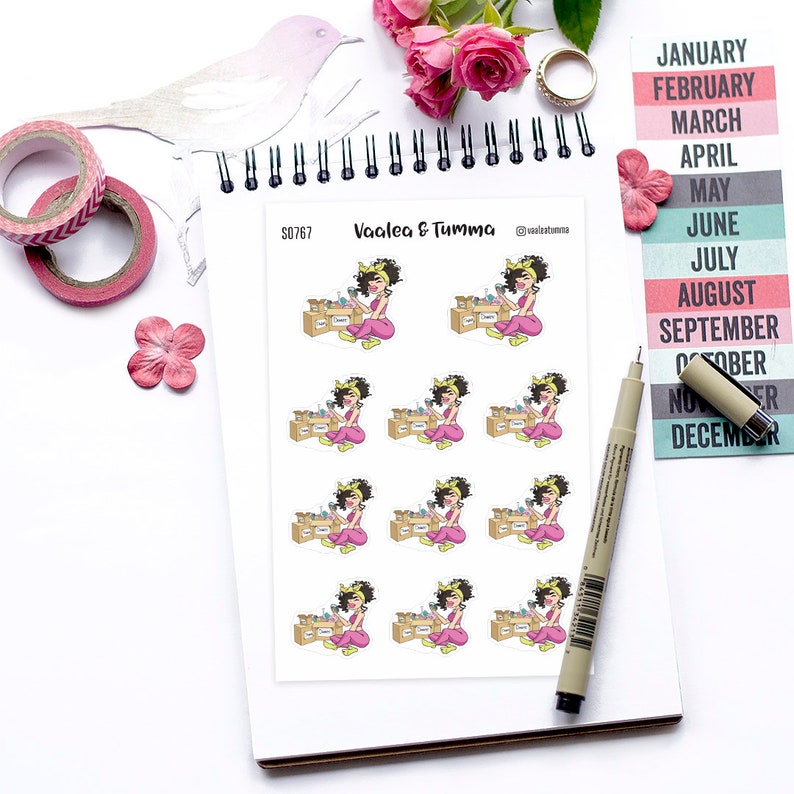 May include: A sheet of stickers featuring a cartoon illustration of a woman with brown hair and a pink outfit. She is holding boxes and has a yellow headband. The stickers are on a white background and have the text "Vaalea & Tumma" and "S0767" printed on them.