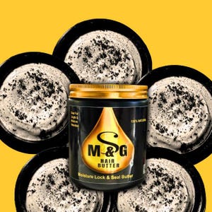May include: A black jar with a gold lid and a gold label that says "M&G Hair Butter Moisture Lock & Seal Butter" with a gold drop design. The jar is surrounded by five white jars with black specks.