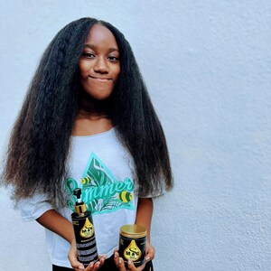 May include: A person with long, black hair is holding two bottles of hair care products. The bottles are black with gold accents and feature the text "M & G Hair Elixir".