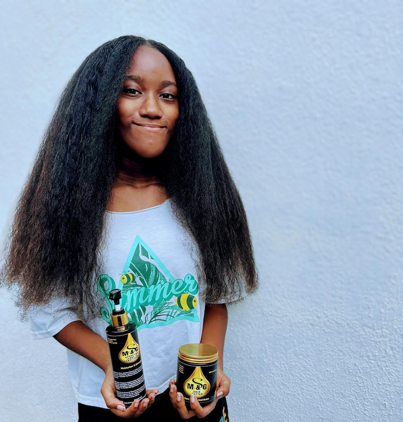 May include: A person with long, black hair is holding two bottles of hair care products. The bottles are black with gold accents and feature the text "M & G Hair Elixir".