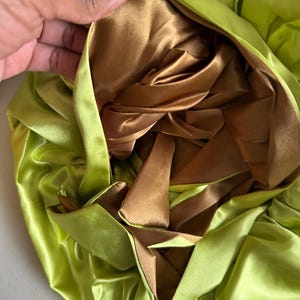 May include: A lime green satin hair bonnet with a brown satin lining. The bonnet is gathered and bunched up, showing the lining.