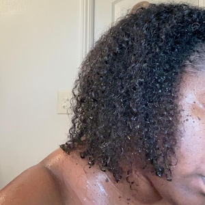 May include: Close-up of a person's dark brown curly hair with a wet look, showing the texture and definition of the curls.