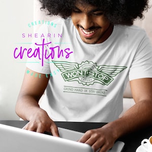 May include: A person wearing a white t-shirt with a green logo that says "Business Expert Won't Stop Grind Hard or Stay Broke". The person is sitting at a table and using a laptop.