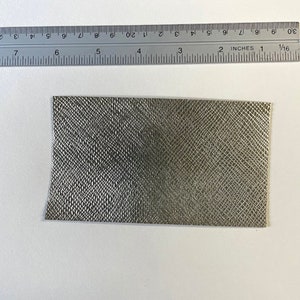 May include: A close-up of a small, rectangular piece of gray fabric with a textured, snake-skin like pattern.