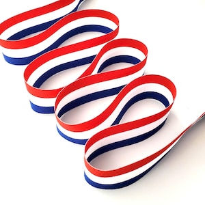 Könnte beinhalten: Band mit roten, weißen und blauen Streifen, in Schleifen angeordnet. Das Band besteht aus einem glatten, gewebten Material. Das Design erinnert an eine Flagge.