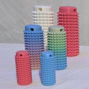 May include: A selection of colourful, cylindrical objects with a textured, studded surface. The objects vary in size and colour, including red, blue, green, and white. Some have a gradient effect. The objects are arranged on a white surface.