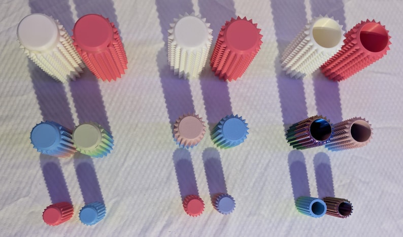 May include: An overhead shot displays several sets of colorful, cylindrical objects with a ridged design. The objects are in various colors, including white, pink, blue, and green. The objects are arranged on a white surface, casting long shadows.