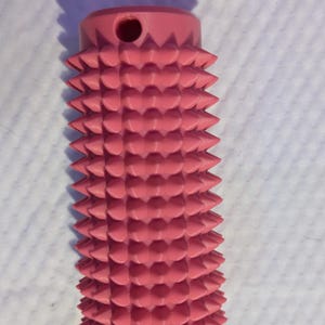 May include: A pink, cylindrical object with a series of conical protrusions. The top of the object has a small hole. The object is likely a massage tool or a similar device.