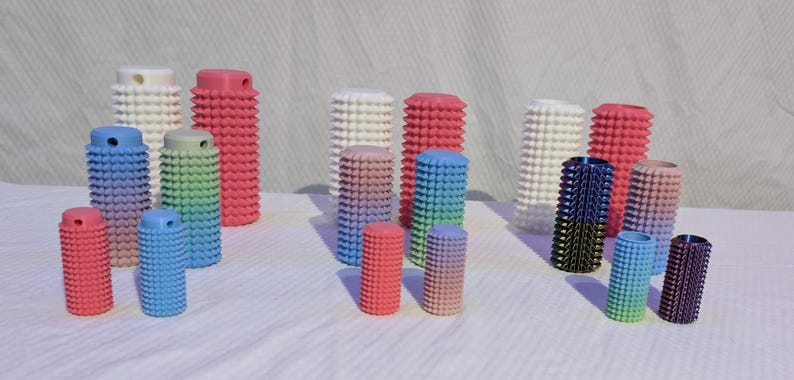 May include: A collection of colorful, cylindrical objects with a textured, studded surface. The objects vary in size and color, including red, blue, green, and white. Some have a gradient effect. The objects are arranged on a white surface.
