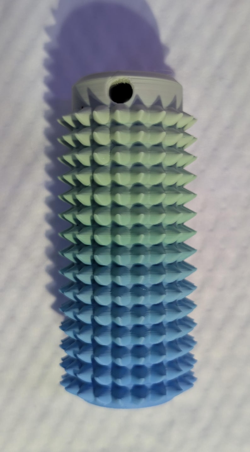 May include: A 3D-printed object with a gradient color scheme, transitioning from light green to blue. The cylindrical shape features a series of conical spikes. The top has a small hole. The object is likely a decorative or functional item.
