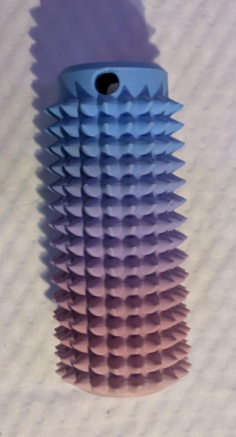 May include: A 3D-printed, gradient-colored object, transitioning from blue to purple to pink. The cylindrical form features a series of conical spikes. A hole is visible at the top. The object is likely a decorative or functional item.