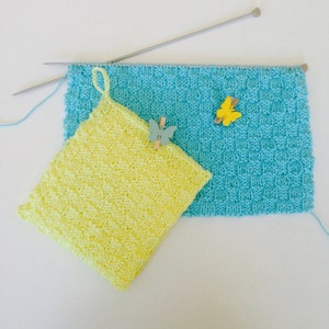 Peut inclure: Deux torchons en tricot, l'un jaune et l'autre bleu, avec une pince à linge en forme de papillon sur chacun. Les torchons sont faits avec un motif de point simple.