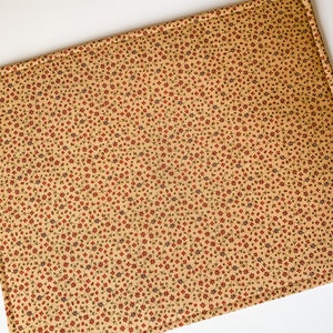 May include: A beige placemat with a small red and blue floral pattern. The placemat has a stitched border.