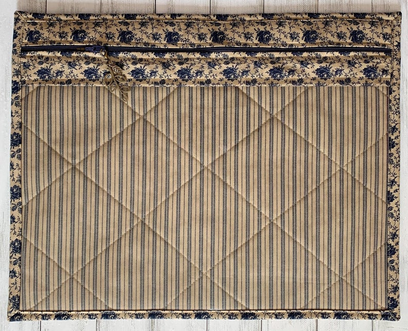 May include: A quilted zippered pouch with a blue and white floral print on the top and bottom edges. The center of the pouch is a tan fabric with vertical blue stripes.