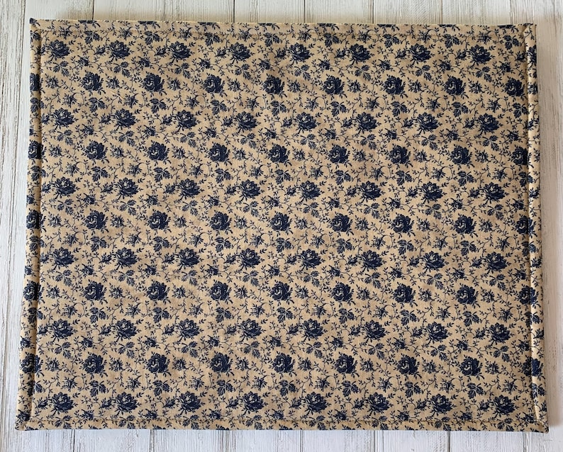 May include: A beige quilted placemat with a navy blue floral pattern.