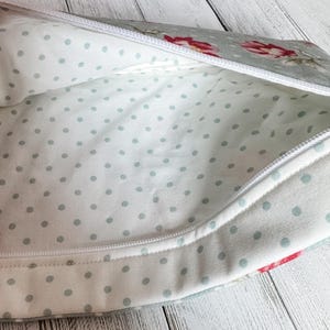 May include: Open view of a floral patterned zippered pouch. The exterior fabric is a light gray with red and pink flowers. The interior is white with small, light blue polka dots. A white zipper runs along the top.