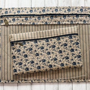 May include: Two zippered pouches made of beige fabric with a black and white floral pattern. The larger pouch has a striped lining and the smaller pouch has a solid beige lining. Both pouches have a zipper closure and a small metal pull tab.
