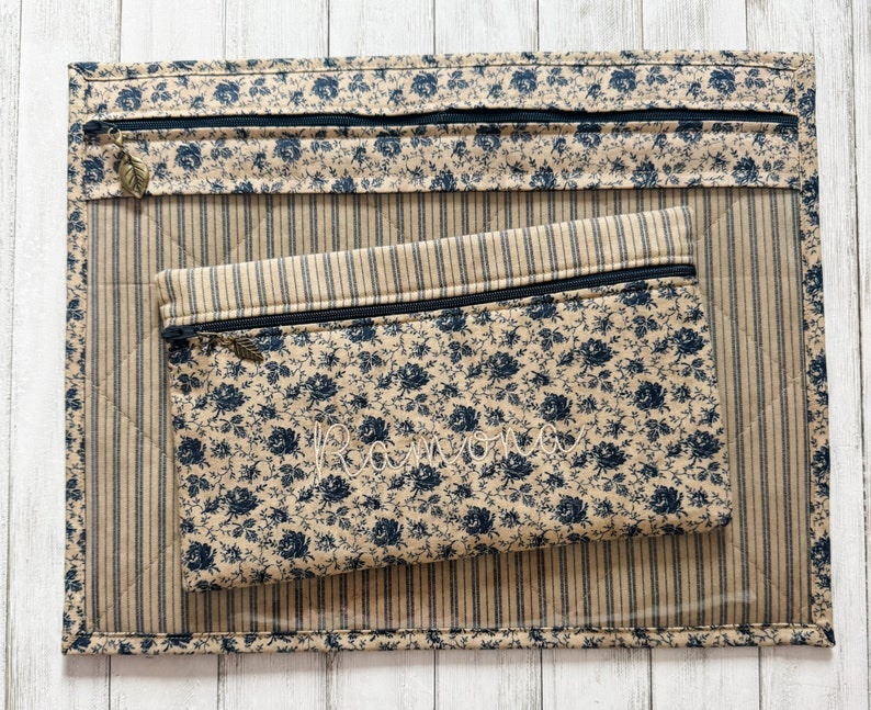 May include: Two zippered pouches made of beige fabric with a black and white floral pattern. The larger pouch has a striped lining and the smaller pouch has a solid beige lining. Both pouches have a zipper closure and a small metal pull tab.