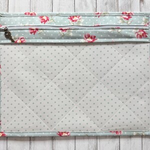 May include: A quilted fabric case with a floral pattern in pink and red on a light blue background. The case has a zipper closure with a key-shaped charm and a dotted interior.