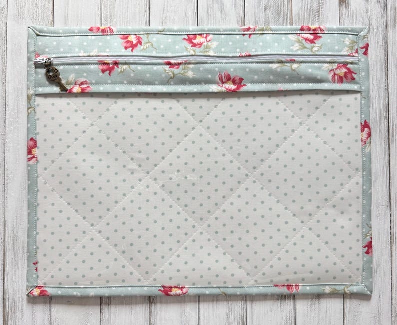 May include: A quilted fabric case with a floral pattern in pink and red on a light blue background. The case has a zipper closure with a key-shaped charm and a dotted interior.