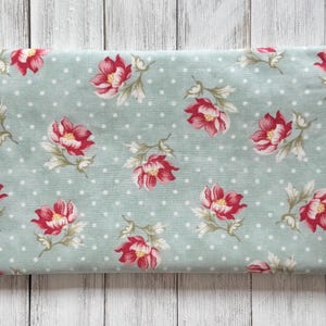 May include: A folded piece of fabric with a floral pattern. The fabric has a light blue background with white polka dots. Large red and pink flowers with green leaves are scattered across the surface.
