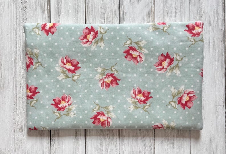 May include: A folded piece of fabric with a floral pattern. The fabric has a light blue background with white polka dots. Large red and pink flowers with green leaves are scattered across the surface.