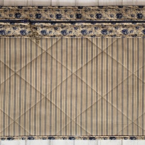 May include: A quilted fabric placemat with a blue and white floral border and a tan and blue striped center.