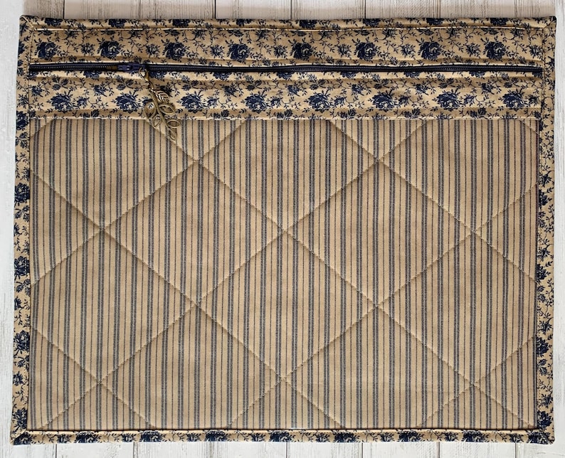 May include: A quilted fabric placemat with a blue and white floral border and a tan and blue striped center.