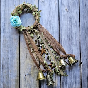 May include: A brown twig wreath with a blue fabric flower and gold bells hanging from brown and beige ribbons.