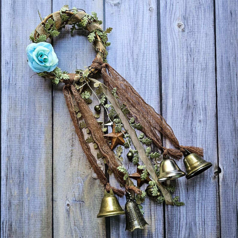 May include: A brown twig wreath with a blue fabric flower and gold bells hanging from brown and beige ribbons.