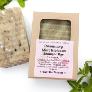 Może przedstawiać: Brązowe pudełko kartonowe z r&oacute;żową etykietą, na kt&oacute;rej widnieje napis "Rosemary Mint Hibiscus Shampoo Bar 4 oz (approx.) Contains saponified oils of coconut, olive, sunflower, castor & grapeseed. "cocoa butter, "hibiscus powder, rosemary & peppermint essential oils organic *Katie Mae Naturals*" Pudełko zawiera kostkę mydła.