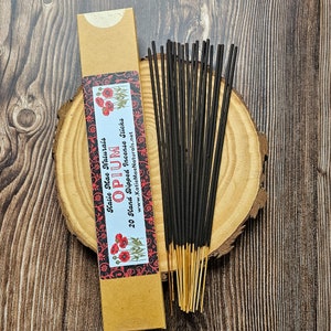 May include: A kraft paper box of 20 hand-dipped incense sticks labeled "Opium" with red poppy illustrations. The incense sticks are black with gold tips, arranged on a wooden slice.