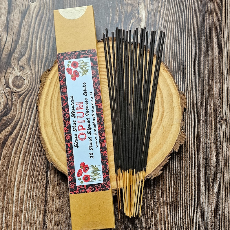 May include: A kraft paper box of 20 hand-dipped incense sticks labeled "Opium" with red poppy illustrations. The incense sticks are black with gold tips, arranged on a wooden slice.