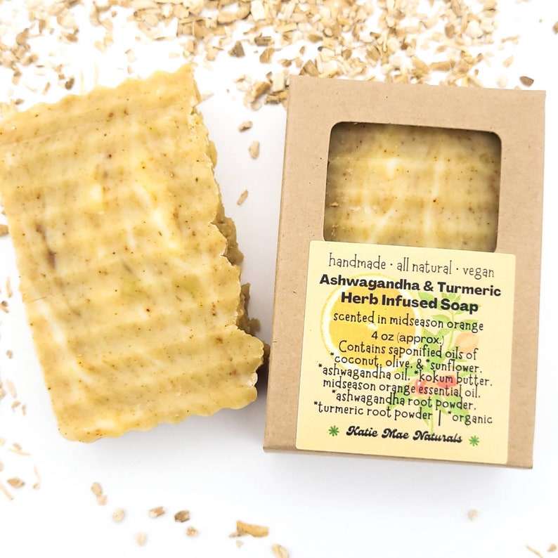 May include: A bar of handmade, all-natural, vegan Ashwagandha & Turmeric Herb Infused Soap, scented in midseason orange. The soap is 4 oz and contains saponified oils of coconut, olive, and sunflower, ashwagandha oil, kokum butter, midseason orange essential oil, ashwagandha root powder, turmeric root powder, and is organic. The soap is packaged in a brown cardboard box with a label that says "Katie Mae Naturals".