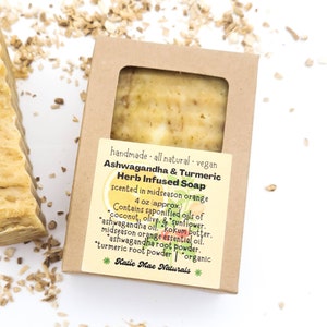 May include: A brown cardboard box with a clear window showing a bar of yellow soap. The label reads "handmade all natural vegan Ashwagandha & Turmeric Herb Infused Soap scented in midseason orange 4 oz (approx.) Contains saponified oils of coconut, olive, & sunflower. ashwagandha oil, kokum butter, midseason orange essential oil, ashwagandha root powder, turmeric root powder | organic *Katie Mae Naturals*"