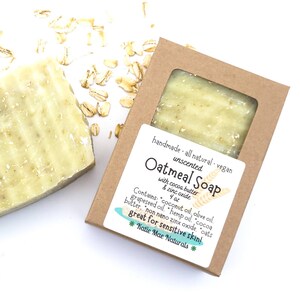 May include: A bar of unscented oatmeal soap with cocoa butter and zinc oxide in a brown cardboard box. The soap is handmade, all-natural, and vegan. The box has a label that says "Oatmeal Soap" with the ingredients and a note that it is "great for sensitive skin!" Katie Mae Naturals.
