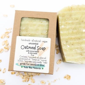 May include: A bar of unscented oatmeal soap in a brown cardboard box. The soap is made with cocoa butter, zinc oxide, coconut oil, olive oil, grapeseed oil, hemp oil, cocoa butter, non-nano zinc oxide, and oats. The label reads "handmade all natural vegan unscented Oatmeal Soap with cocoa butter & zinc oxide 4 oz Contains: coconut oil, olive oil, grapeseed oil, hemp oil, cocoa butter, non nano zinc oxide, oats great for sensitive skin! *Katie Mae Naturals*"