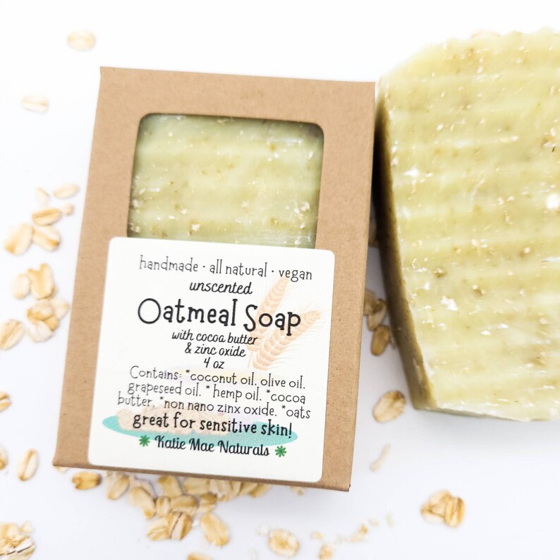 May include: A bar of unscented oatmeal soap in a brown cardboard box. The soap is made with cocoa butter, zinc oxide, coconut oil, olive oil, grapeseed oil, hemp oil, cocoa butter, non-nano zinc oxide, and oats. The label reads "handmade all natural vegan unscented Oatmeal Soap with cocoa butter & zinc oxide 4 oz Contains: coconut oil, olive oil, grapeseed oil, hemp oil, cocoa butter, non nano zinc oxide, oats great for sensitive skin! *Katie Mae Naturals*"