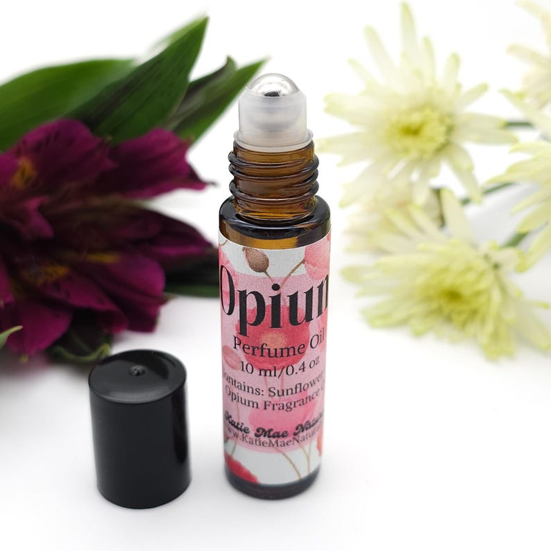 Puede incluir: Un frasco de vidrio con un tap&oacute;n negro y una etiqueta rosa y blanca que dice "Opium Perfume Oil 10 ml/0.4 oz Contains: Sunflower Opium Fragrance Katie Mae Naturals www.KatieMaeNaturals.com"