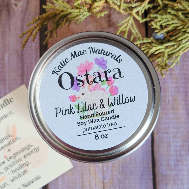 Peut inclure: Une bougie en cire de soja de 170 grammes dans une bo&icirc;te en &eacute;tain argent&eacute;e avec une &eacute;tiquette blanche. L'&eacute;tiquette pr&eacute;sente un motif floral et le texte "Katie Mae Naturals Ostara Pink Lilac & Willow Hand Poured Soy Wax Candle phthalate free 6 oz".