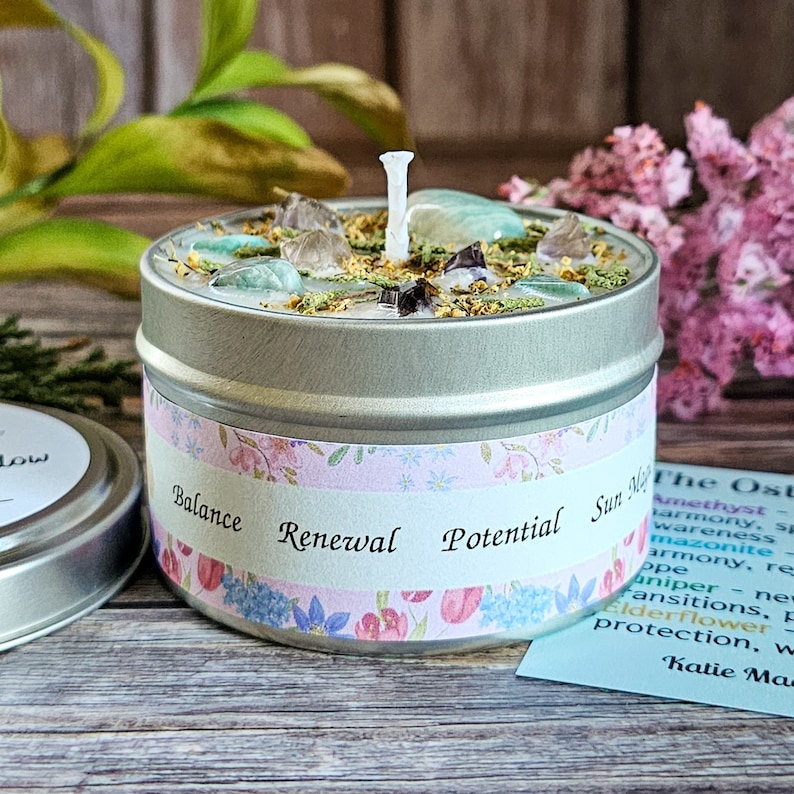 Peut inclure: Une bougie en bo&icirc;te argent&eacute;e avec un motif floral et les mots "Balance Renewal Potential Sun" sur l'&eacute;tiquette. La bougie est entour&eacute;e de fleurs vertes et roses et a une m&egrave;che blanche.