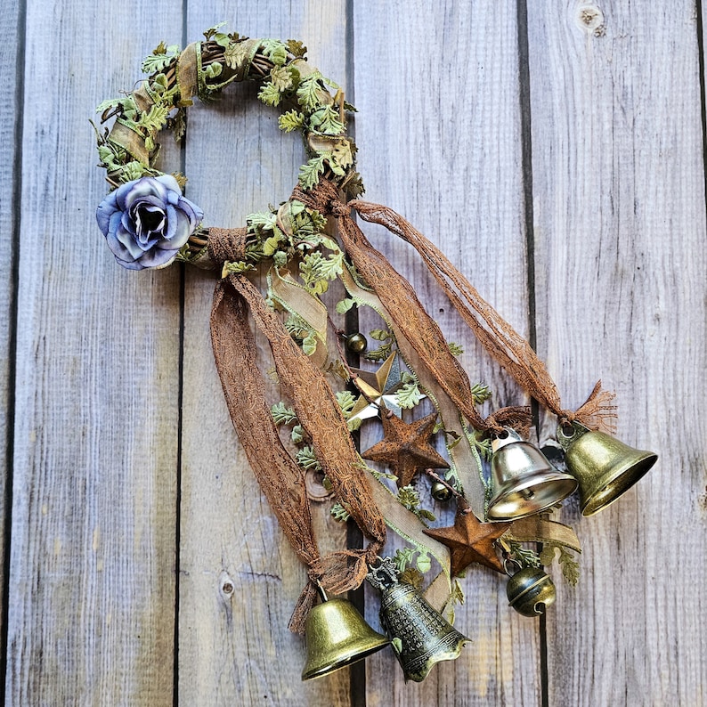 May include: A green and brown wreath with a blue flower and brown ribbon, decorated with bells and stars.
