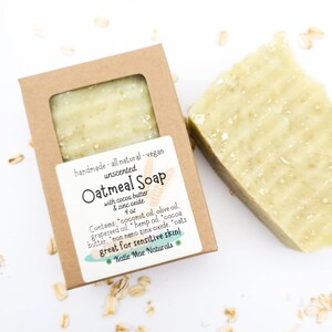 May include: A brown cardboard box with a clear window showing a bar of oatmeal soap. The label reads "handmade all natural. vegan unscented Oatmeal Soap with cocoa butter & zinc oxide 4 oz Contains "coconut oil, olive oil. grapeseed oil. hemp oil. cocoa butter, "non nano zinx oxide. "oats great for sensitive skin! *Katie Mae Naturals *"
