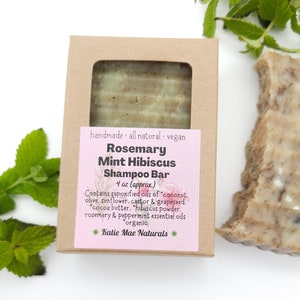 Może przedstawiać: Brązowe pudełko kartonowe z r&oacute;żową etykietą, na kt&oacute;rej widnieje napis "Rosemary Mint Hibiscus Shampoo Bar 4 oz (approx) Contains saponified oils of "coconut, olive, sunflower, castor & grapeseed. "cocoa butter, "hibiscus powder. rosemary & peppermint essential oils organic *Katie Mae Naturals*"