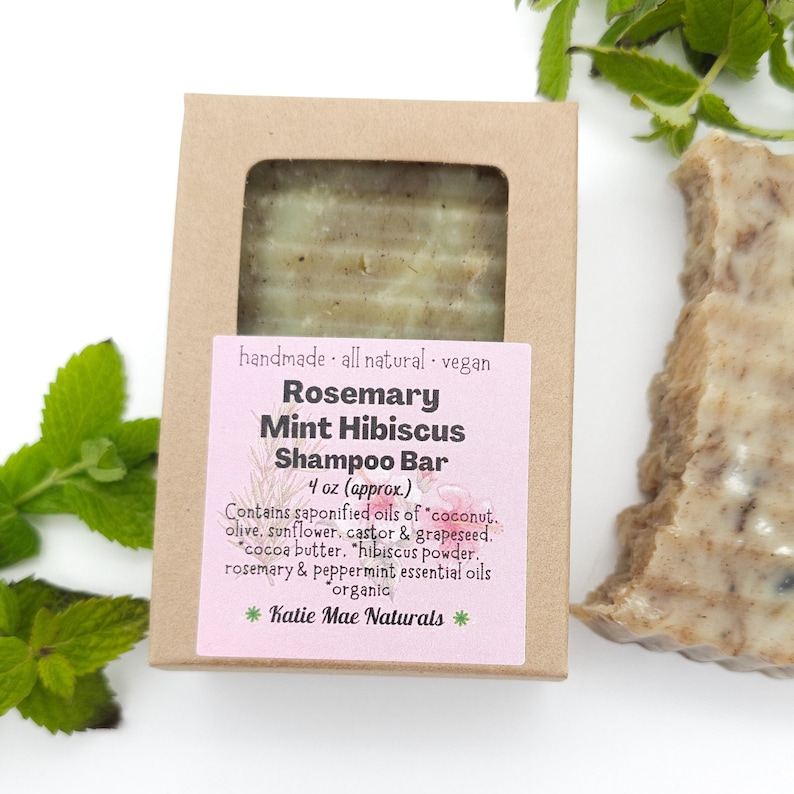 Może przedstawiać: Brązowe pudełko kartonowe z r&oacute;żową etykietą, na kt&oacute;rej widnieje napis "Rosemary Mint Hibiscus Shampoo Bar 4 oz (approx) Contains saponified oils of "coconut, olive, sunflower, castor & grapeseed. "cocoa butter, "hibiscus powder. rosemary & peppermint essential oils organic *Katie Mae Naturals*"